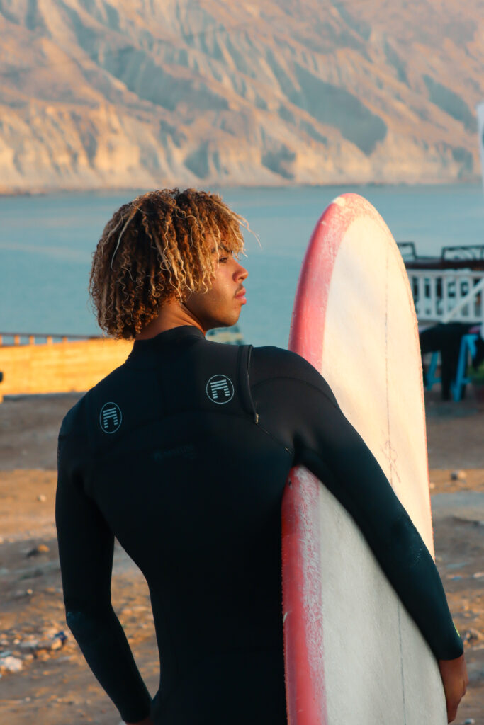 Backview portrait of Amouddou Surf's founder holding one of his surfboards.